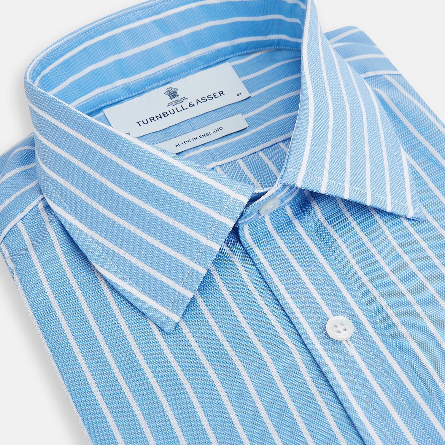 View 2 of product The Turnbull & Asser Sky Blue Wide Pinstripe Mayfair Shirt features long sleeves, a classic collar, and buttoned cuffs, laid flat against a white background for a refined formal look.