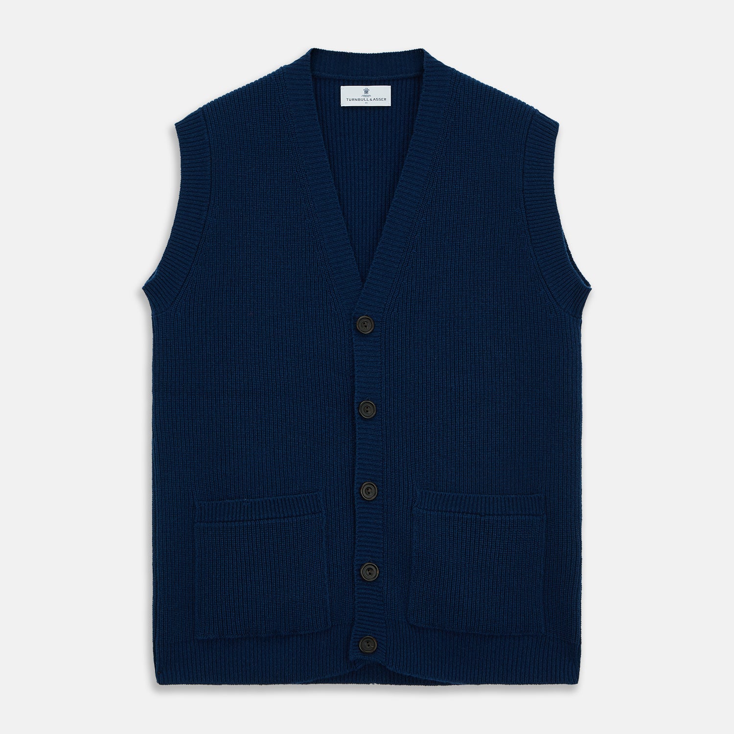 View 2 of product A man with a shaved head wears a Turnbull & Asser Navy Sleeveless Cashmere Cardigan over a white dress shirt with rolled-up sleeves and dark trousers, standing against a plain light gray background.