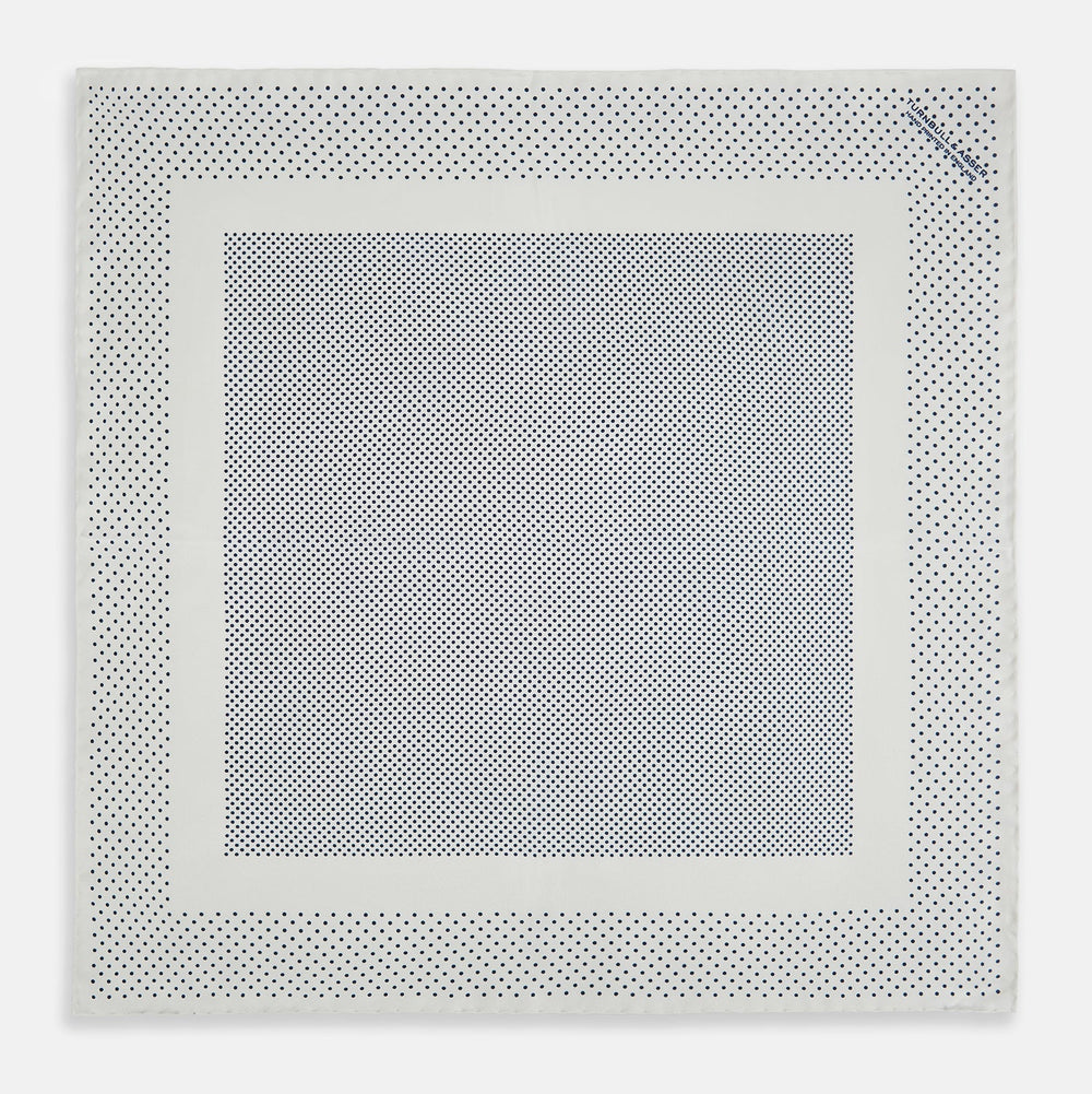 The Turnbull & Asser Cream Dot Silk Pocket Square features a neatly folded pure silk design with a border and center pattern of small navy blue polka dots, displayed on a plain white background.