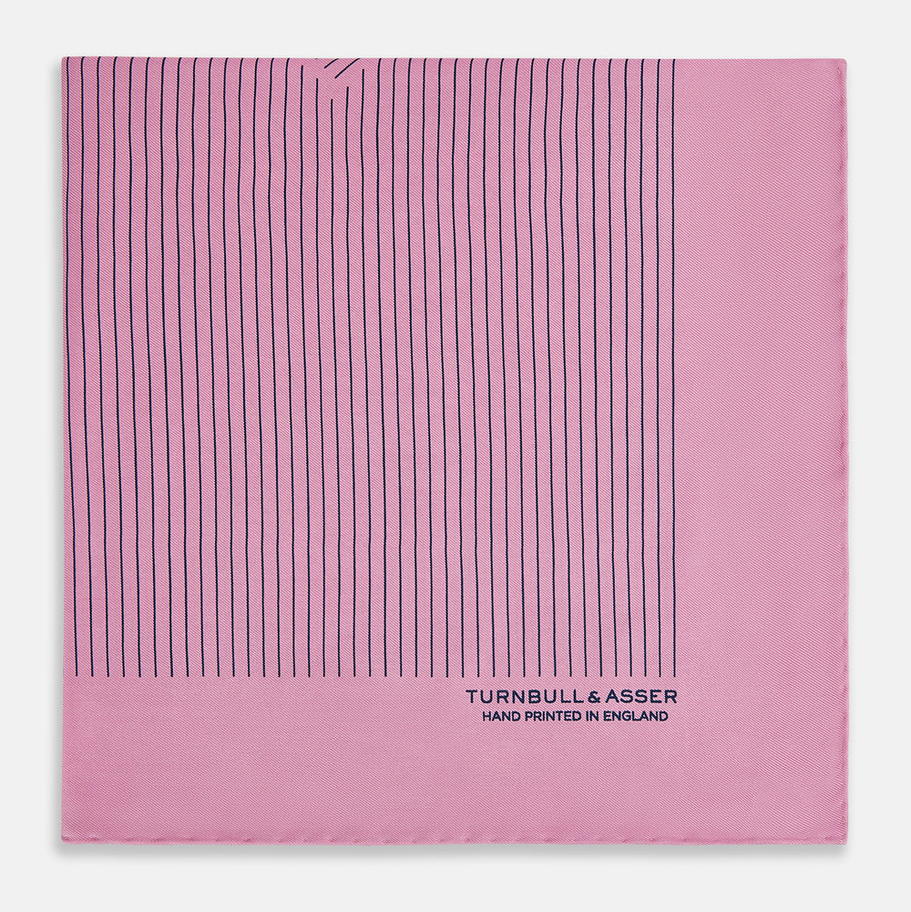 The Turnbull & Asser Pink Stripe Silk Pocket Square features thin vertical navy stripes and "TURNBULL & ASSER HAND PRINTED IN ENGLAND" in the bottom right corner, with one corner stylishly folded over.