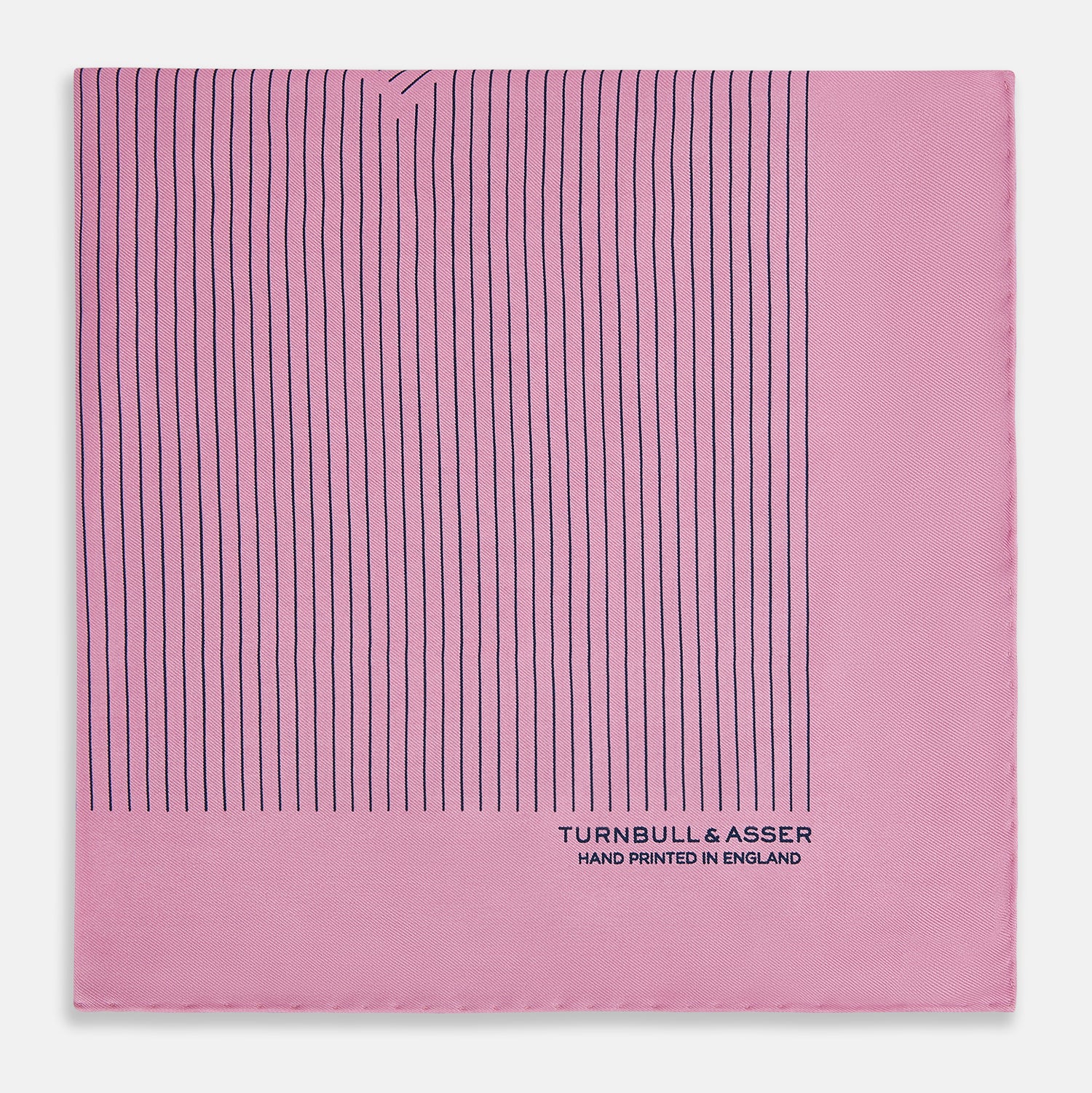 View 4 of product The Turnbull & Asser Pink Stripe Silk Pocket Square features thin vertical navy stripes and "TURNBULL & ASSER HAND PRINTED IN ENGLAND" in the bottom right corner, with one corner stylishly folded over.