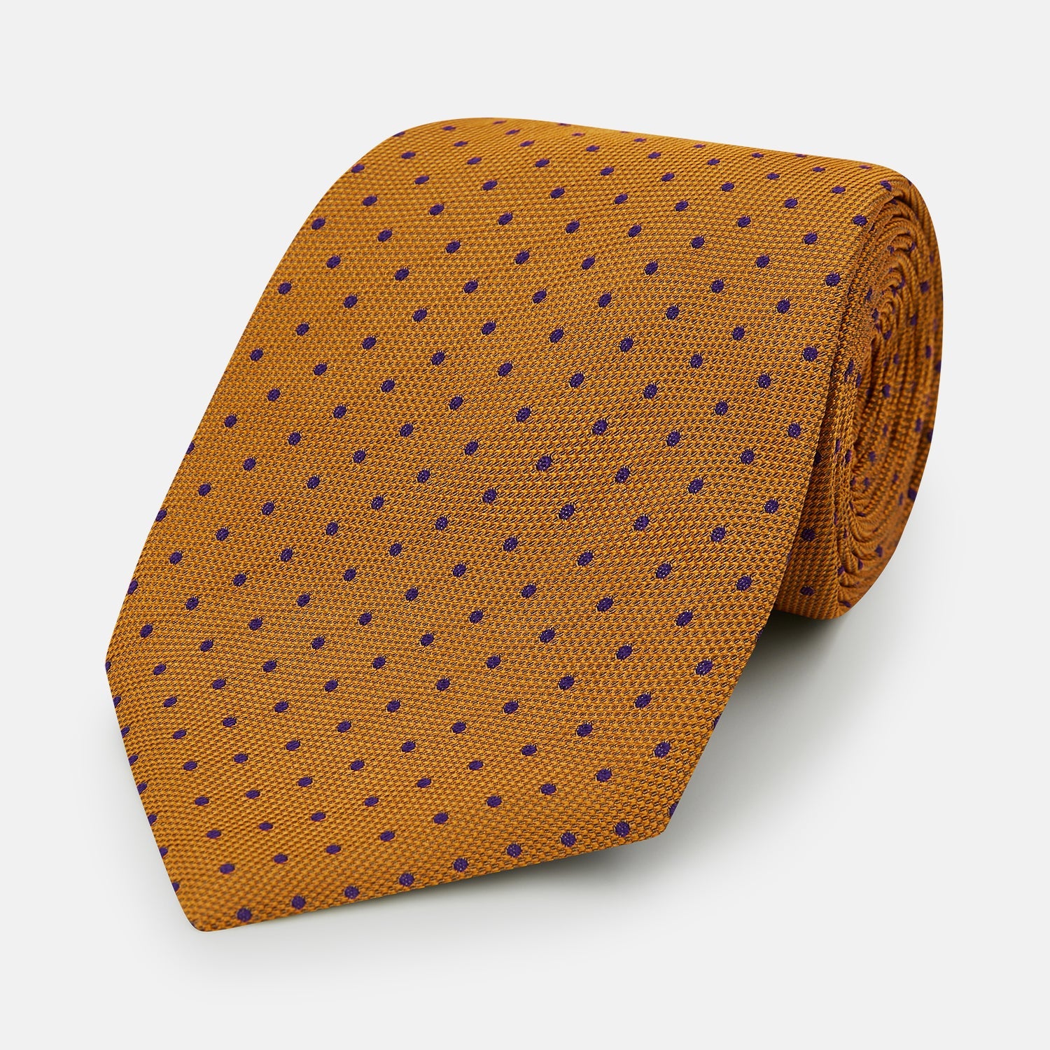 View 1 of product The Turnbull & Asser Purple and Orange Micro Dot Silk Tie features a pattern of small blue dots, shown rolled up on a white background.