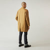 View 4 of product A person wears the Turnbull & Asser Camel Quintern Sealup Raincoat with Detachable Liner, paired with dark pants, standing against a plain light gray background, showing the sleek technical rainwear style with one hand in a pocket.