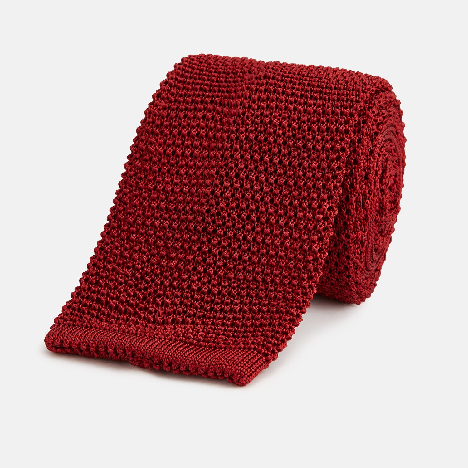 View 1 of product The Turnbull & Asser KNITTED RED SILK PLAIN TIE, featuring a textured finish, is rolled up and displayed against a plain white background.