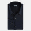 View 5 of product The Midnight Blue Hyde Overshirt by Turnbull & Asser is a plain, long-sleeve shirt in dark navy sanforised cotton with a single chest pocket, spread collar, and black buttons, shown laid flat on a white background.