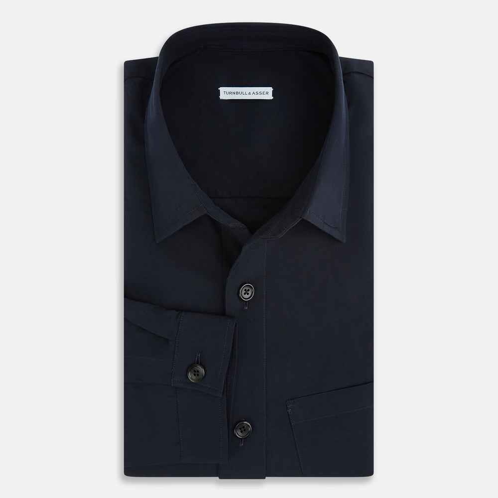 The Midnight Blue Hyde Overshirt by Turnbull & Asser is a plain, long-sleeve shirt in dark navy sanforised cotton with a single chest pocket, spread collar, and black buttons, shown laid flat on a white background.