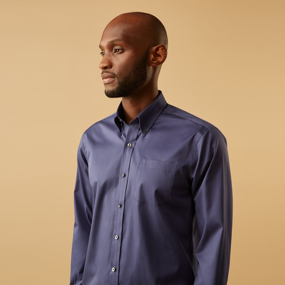 The Blue Piece Dyed Weekend Fit Suffolk Shirt by Turnbull & Asser features a button-down Dorset collar, chest pocket, white buttons, and long sleeves in classic navy, laid flat against a white background.