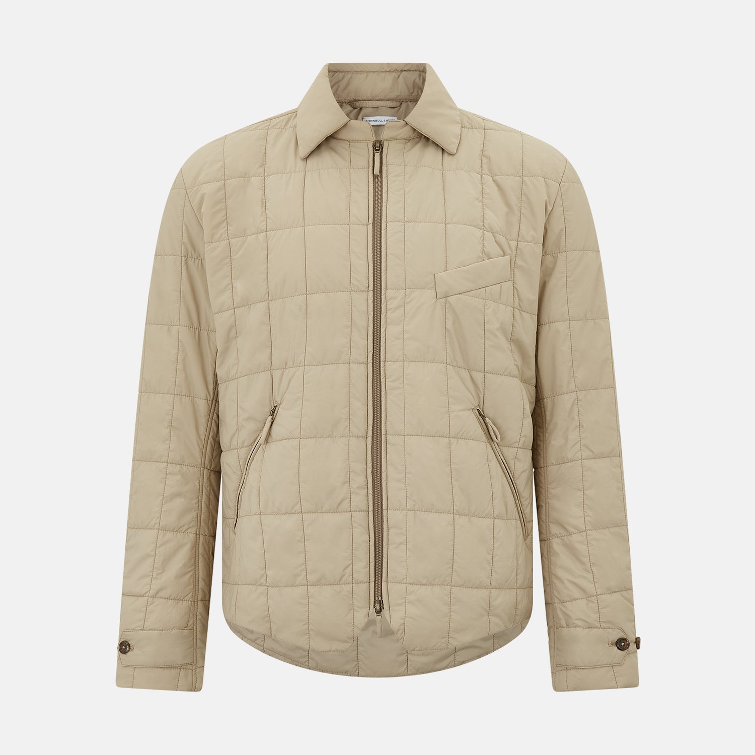 View 1 of product The Battersea Sand Quilted Jacket by Turnbull & Asser is a light beige men's jacket with a front zipper, pointed collar, zippered side pockets, chest pocket, and buttoned cuffs, shown on a plain white background.