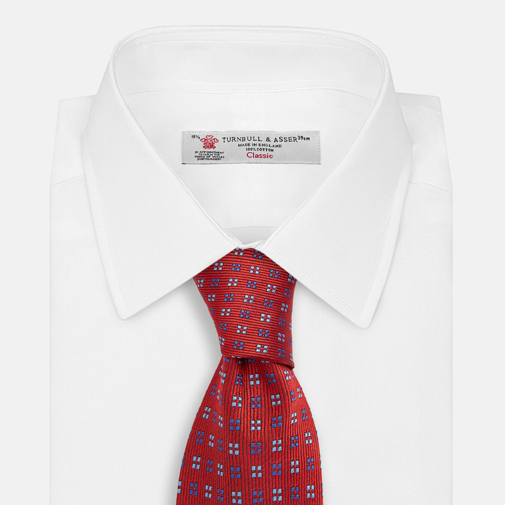 The Turnbull & Asser MINI SQUARE SPOT TULIP RED BLUE TIE features a vivid red base with blue and white geometric spots, making it a stylish addition to any refined ensemble.