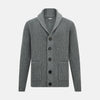 View 1 of product The Turnbull & Asser Grey Melange Cashmere Shawl Collar Cardigan features a ribbed-knit texture, five black front buttons, and two pockets, shown against a plain white background.