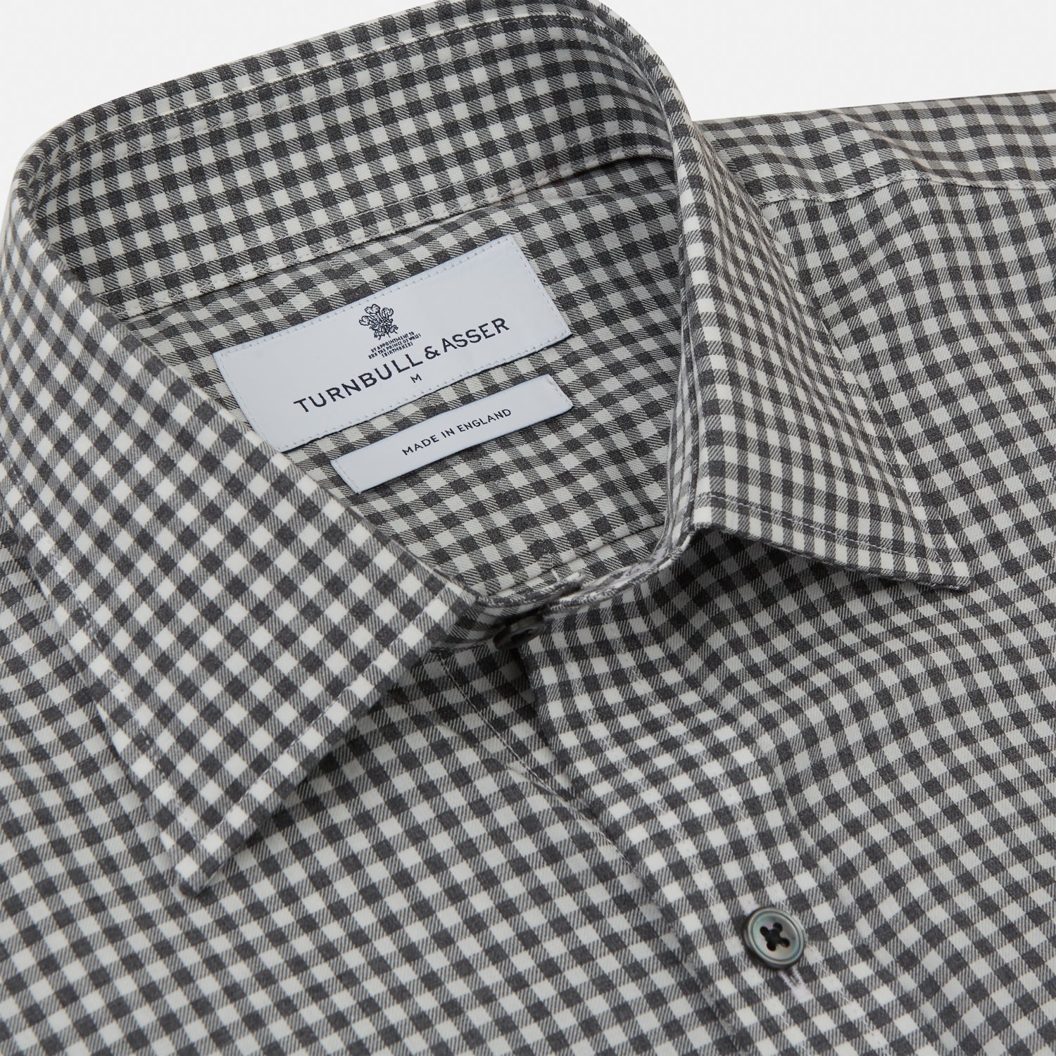 View 3 of product A person with a shaved head models the Turnbull & Asser Grey Check Weekend Fit Flannel Shirt with a Derby collar and 1-button cuffs, sleeves rolled up, paired with dark trousers against a plain background, gazing directly at the camera.