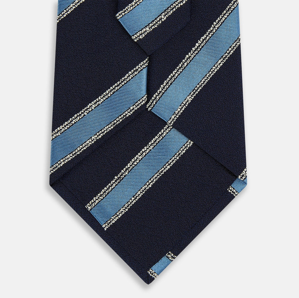 The Turnbull & Asser Navy Multi Stripe Silk Tie features diagonal light blue and silver stripes on an English silk navy base, rolled neatly against a white background.