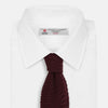 View 2 of product The Turnbull & Asser Knitted Burgundy Square Silk Plain Tie, featuring a textured open-weave pattern, is rolled up and displayed on a plain white background—a versatile accessory for the modern gentleman.