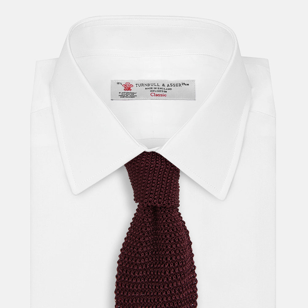 The Turnbull & Asser Knitted Burgundy Square Silk Plain Tie, featuring a textured open-weave pattern, is rolled up and displayed on a plain white background—a versatile accessory for the modern gentleman.