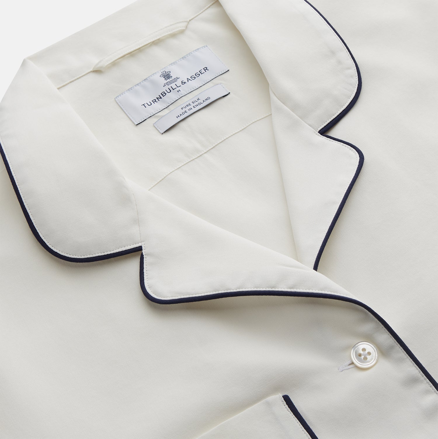 View 3 of product The Women's Harriet Cream Silk Pyjama Set by Turnbull & Asser features a white sand-washed silk button-up top with black piping and chest pocket, plus matching drawstring pants, all shown against a white background.