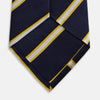 View 4 of product The Yellow and White Blazer Silk Tie by Turnbull & Asser, featuring diagonal white and yellow stripes on navy blue, is shown rolled up against a light gray background.