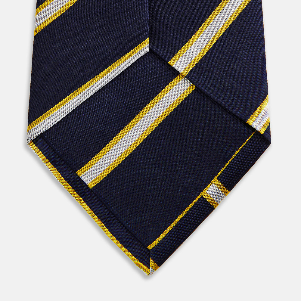 The Yellow and White Blazer Silk Tie by Turnbull & Asser, featuring diagonal white and yellow stripes on navy blue, is shown rolled up against a light gray background.