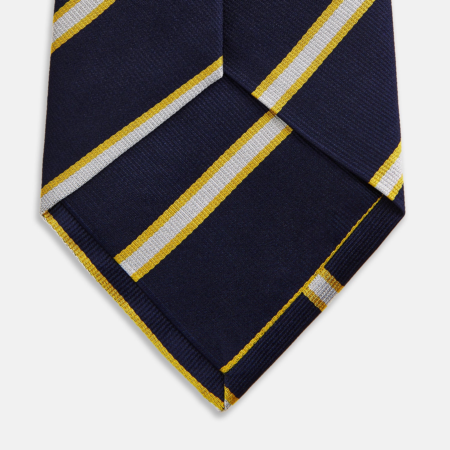 View 4 of product The Yellow and White Blazer Silk Tie by Turnbull & Asser, featuring diagonal white and yellow stripes on navy blue, is shown rolled up against a light gray background.