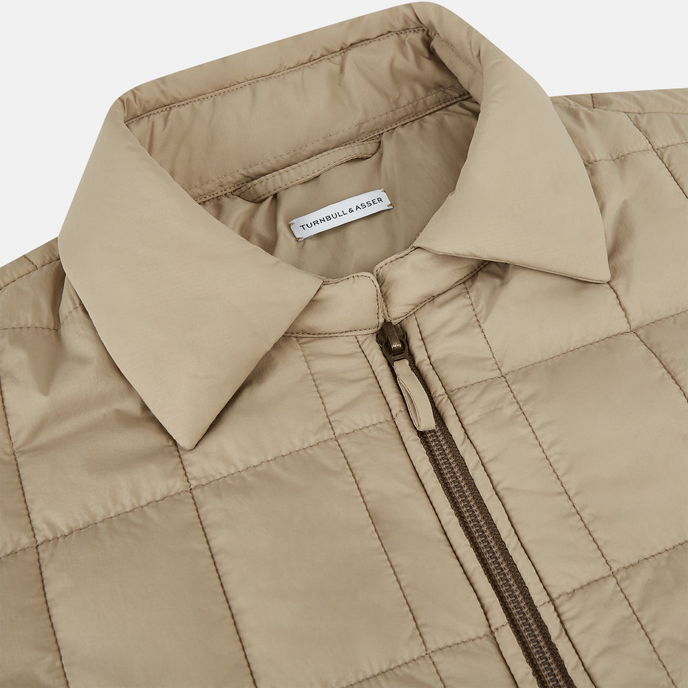 The Battersea Sand Quilted Jacket by Turnbull & Asser is a light beige men's jacket with a front zipper, pointed collar, zippered side pockets, chest pocket, and buttoned cuffs, shown on a plain white background.