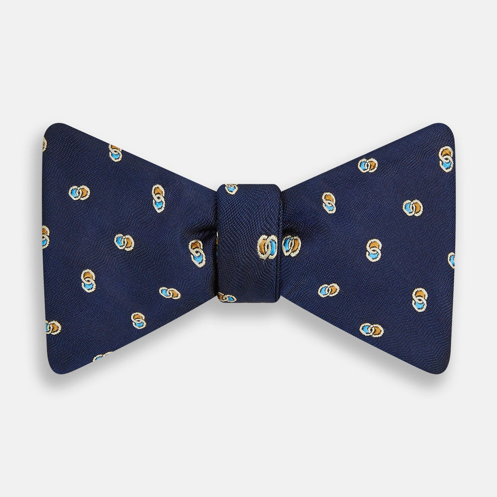 The Blue and Yellow Links Silk Bow Tie by Turnbull & Asser features a subtle wavy texture with a refined pattern of interlinked gold, blue, and white rings—an elegant accessory to enhance any formal outfit.