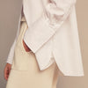 View 4 of product A woman with straight brown hair pulled back wears the Turnbull & Asser White Cotton Marlene Shirt, featuring classic menswear details, paired with high-waisted cream trousers against a neutral background.