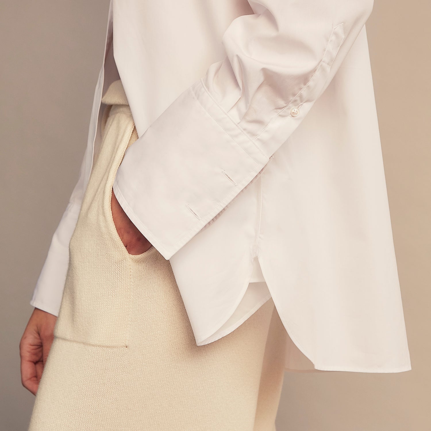 View 4 of product A woman with straight brown hair pulled back wears the Turnbull & Asser White Cotton Marlene Shirt, featuring classic menswear details, paired with high-waisted cream trousers against a neutral background.