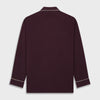 View 5 of product The Turnbull & Asser Plain Plum Silk Modern Pyjama Set, made in England, features white piping, a button-up long-sleeve top with three pockets, and matching pants. The pyjamas are shown against a white background.