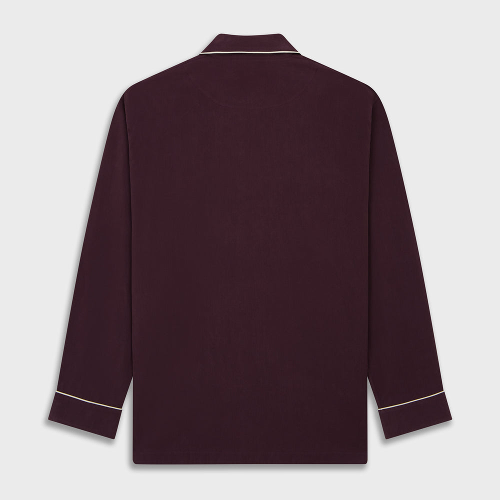 The Turnbull & Asser Plain Plum Silk Modern Pyjama Set, made in England, features white piping, a button-up long-sleeve top with three pockets, and matching pants. The pyjamas are shown against a white background.