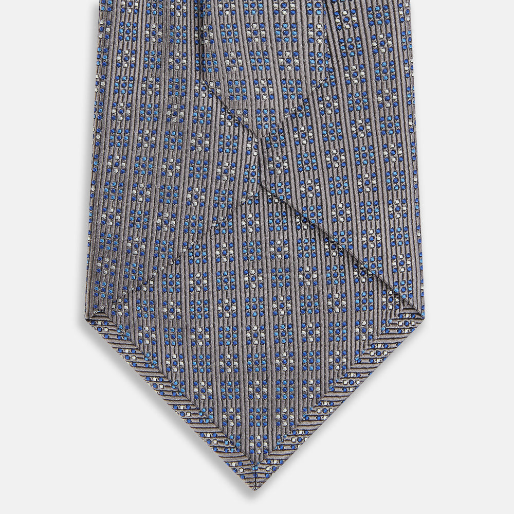 The Turnbull & Asser Silver and Pale Blue Multi Dot Silk Tie features elegant small dots on light brown silk, ideal for modern office wear, shown rolled up against a white background.