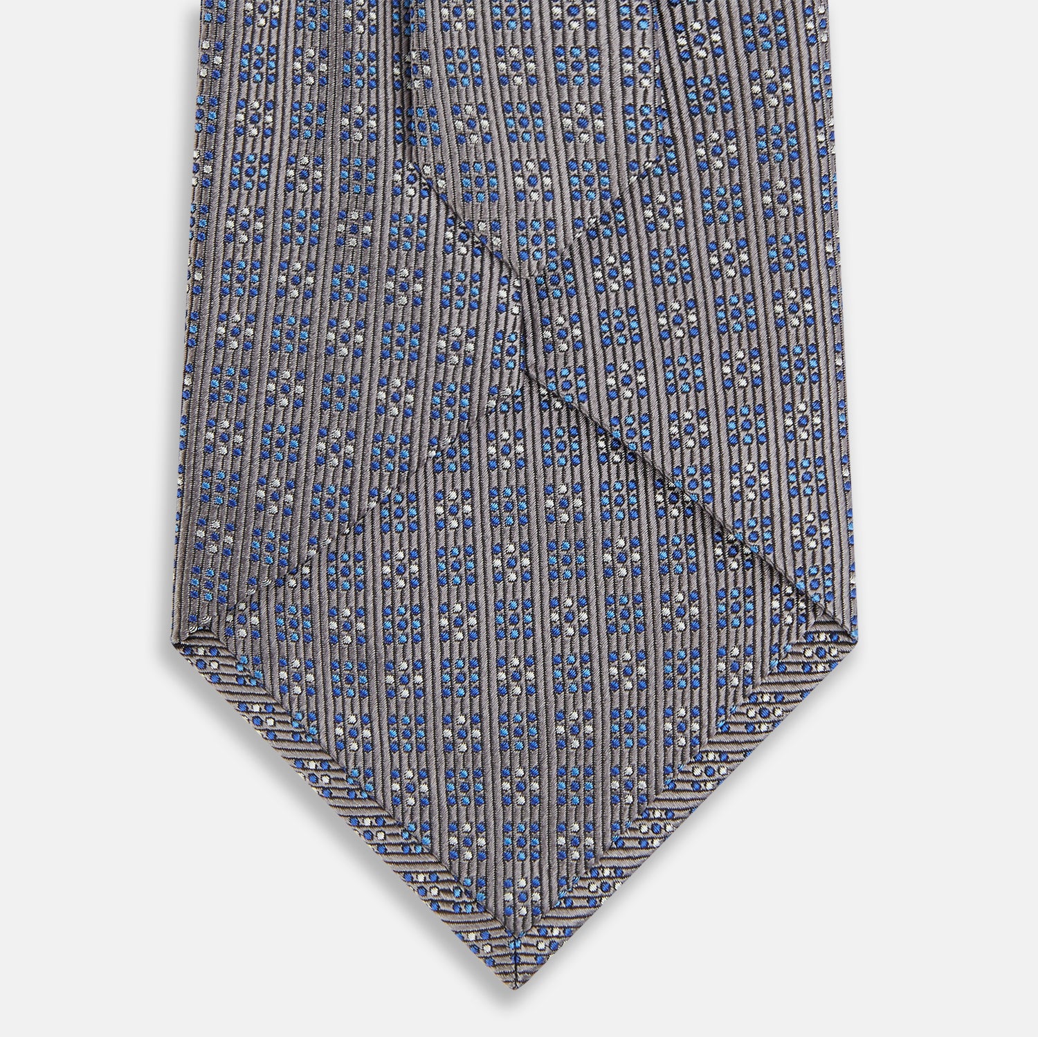 View 3 of product The Turnbull & Asser Silver and Pale Blue Multi Dot Silk Tie features elegant small dots on light brown silk, ideal for modern office wear, shown rolled up against a white background.