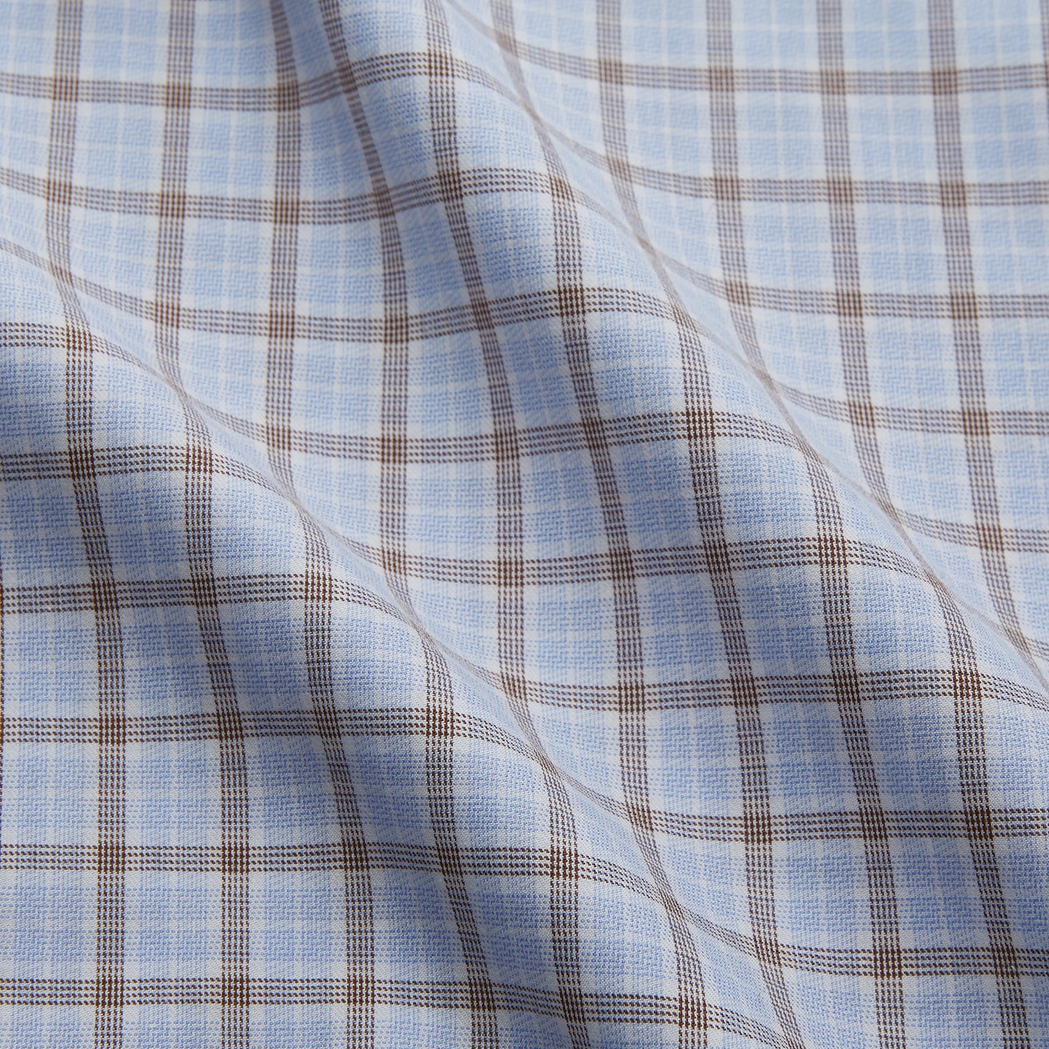 View 4 of product A man wearing glasses and a Pale Blue Multi Check Cashmerello Holiday Fit Winnington Shirt by Turnbull & Asser leans casually against a white countertop, looking at the camera with a neutral expression.