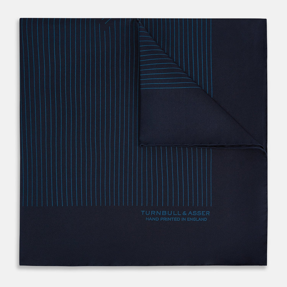 The Navy and Blue Stripe Silk Pocket Square by Turnbull & Asser features vertical blue pinstripes, is crafted from silk with hand-rolled edges, and is finished with the brand's logo printed in blue at the lower right corner.