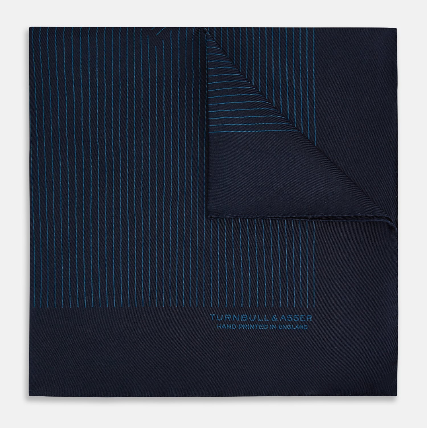 View 1 of product The Navy and Blue Stripe Silk Pocket Square by Turnbull & Asser features vertical blue pinstripes, is crafted from silk with hand-rolled edges, and is finished with the brand's logo printed in blue at the lower right corner.