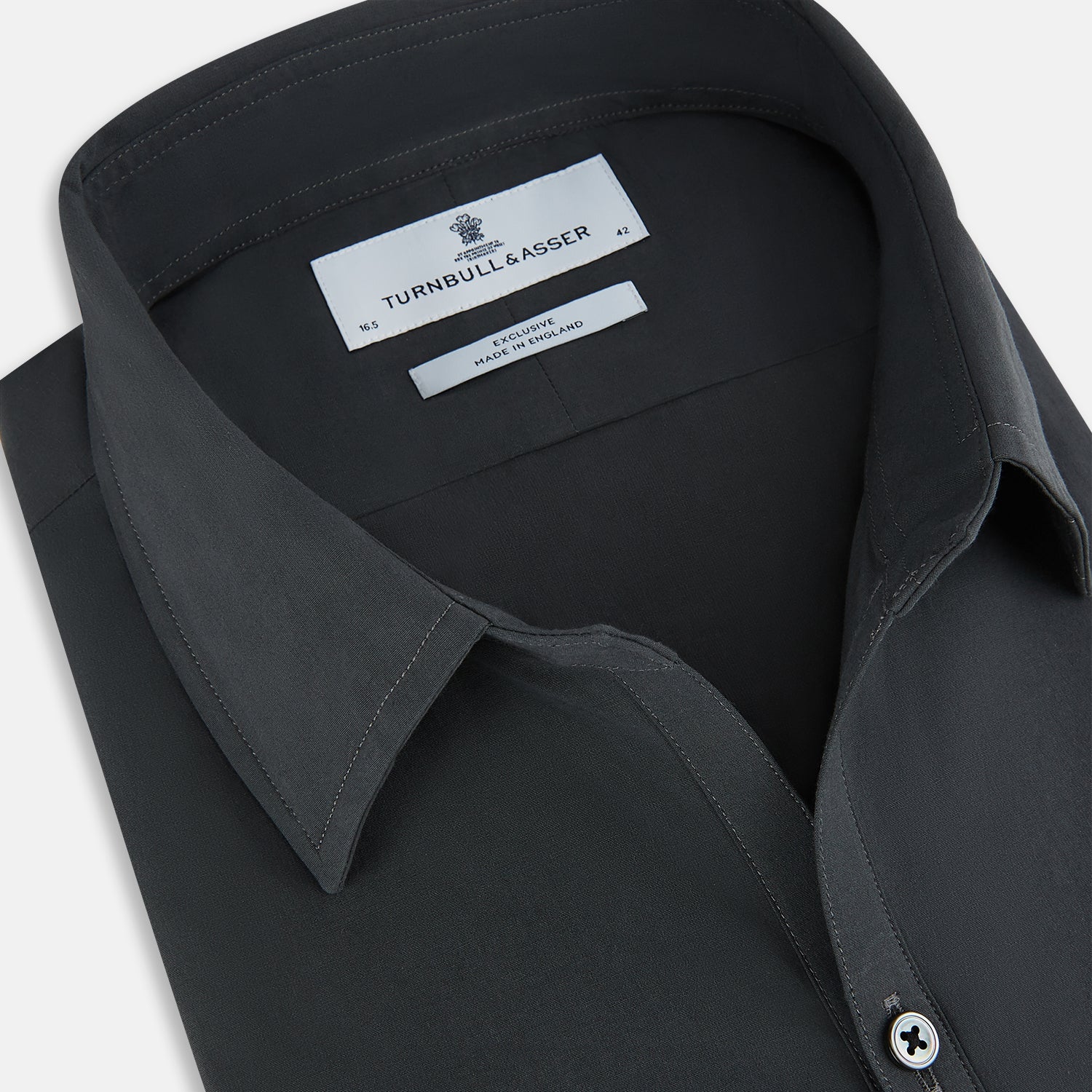 View 2 of product The Charcoal Windsor Shirt by Turnbull & Asser is a black, long-sleeve button-up with a pointed Windsor collar, buttoned cuffs, and a straight hem, shown flat on a white background.