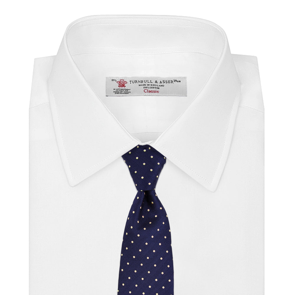 The Turnbull & Asser Navy Spot Woven Herringbone Silk Tie features a navy blue base with evenly spaced yellow polka dots, making it an essential accessory for smart attire. Displayed rolled on a white background.