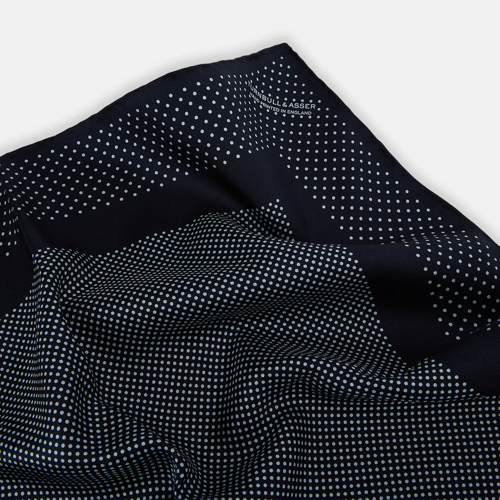 The Turnbull & Asser Navy and Light Blue Dot Silk Pocket Square features white polka dots, a contrasting border, and an inner square design, showcasing handmade craftsmanship with its expertly folded finish.