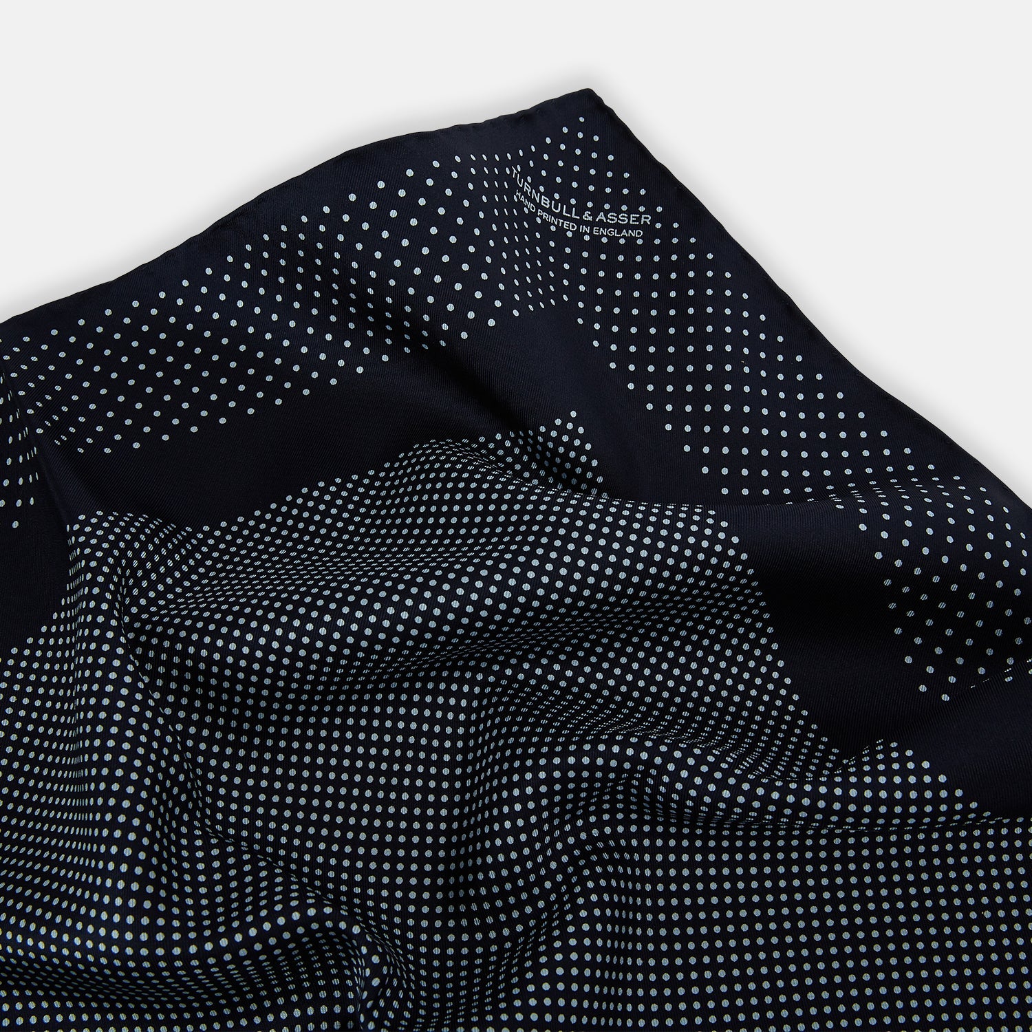 View 2 of product The Turnbull & Asser Navy and Light Blue Dot Silk Pocket Square features white polka dots, a contrasting border, and an inner square design, showcasing handmade craftsmanship with its expertly folded finish.