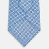 View 3 of product The Turnbull & Asser Blue Floral Tile Pattern Printed Silk Tie features a light blue geometric and floral design in dark blue, shown rolled up on a white background.