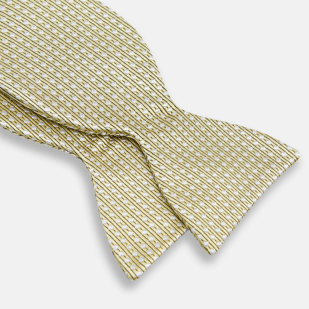 The Turnbull & Asser Gold and White Square Silk Bow Tie features a textured design with square patterns, ideal for formalwear, and is elegantly presented on a white background.