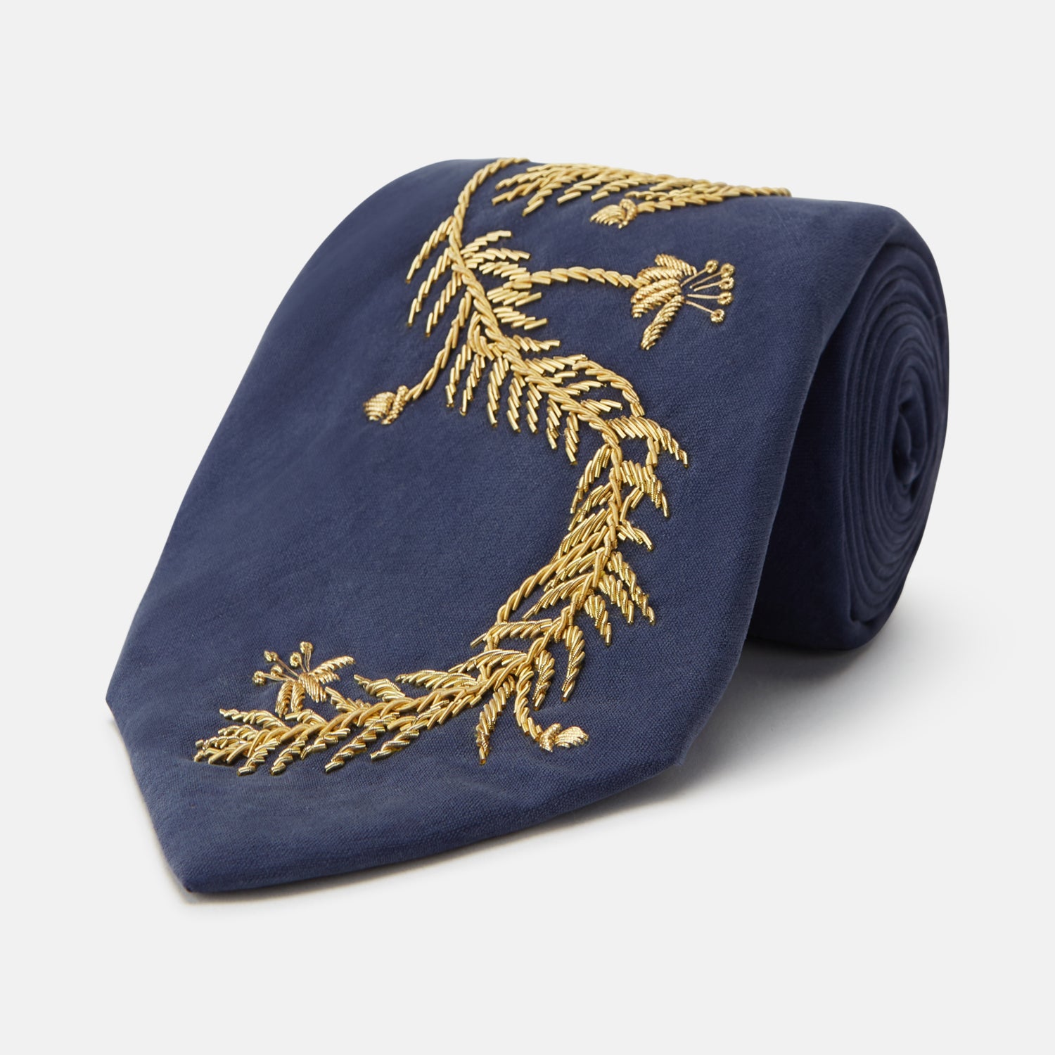 View 1 of product The Turnbull & Asser Navy Gold Embroidered Botanical Tie features intricate gold botanical embroidery on navy blue silk, neatly rolled with the detailed tip facing forward.