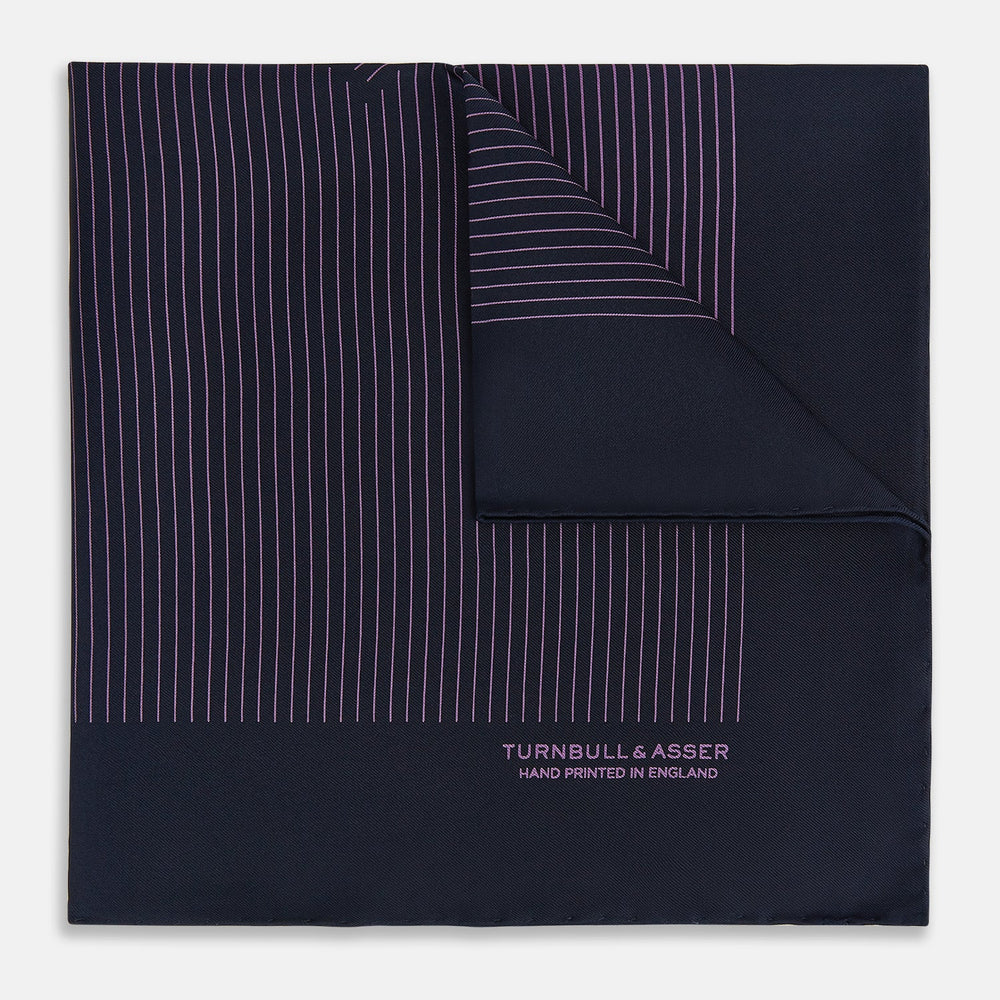 A navy silk pocket square with thin, even purple stripes and hand-rolled edges from Turnbull & Asser, featuring "Turnbull & Asser Hand Printed in England" printed in the corner.