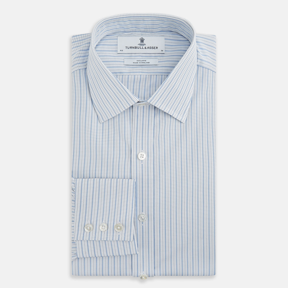 The Turnbull & Asser Blue Graph Check Mayfair Shirt features a classic T&A collar, Mayfair fit, buttoned cuffs, and long sleeves with light blue graph checks on a white background.