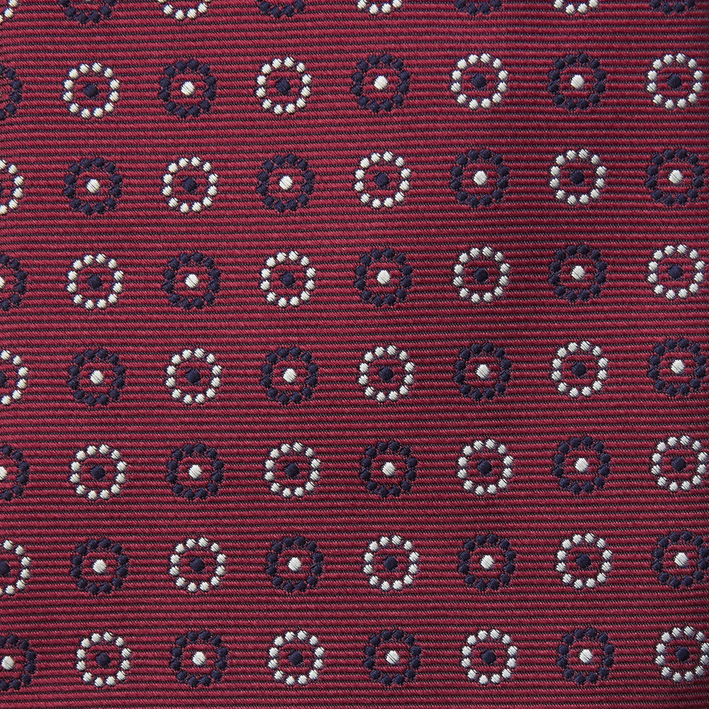 The Red Spheric Emblem Tie by Turnbull & Asser is a rolled-up maroon silk tie with a jacquard pattern of small white and purple circular dots, shown against a white background.