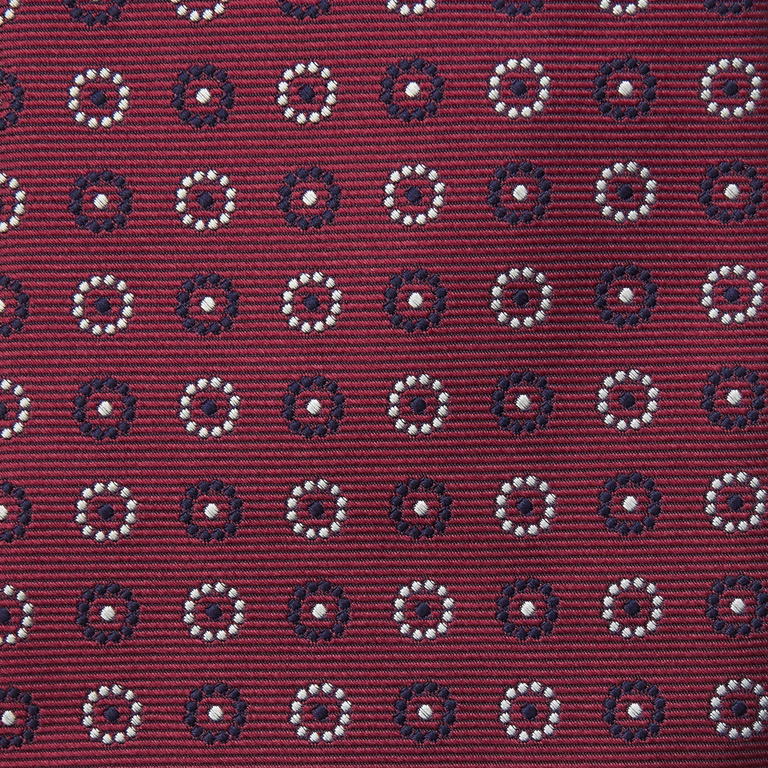 View 3 of product The Red Spheric Emblem Tie by Turnbull & Asser is a rolled-up maroon silk tie with a jacquard pattern of small white and purple circular dots, shown against a white background.