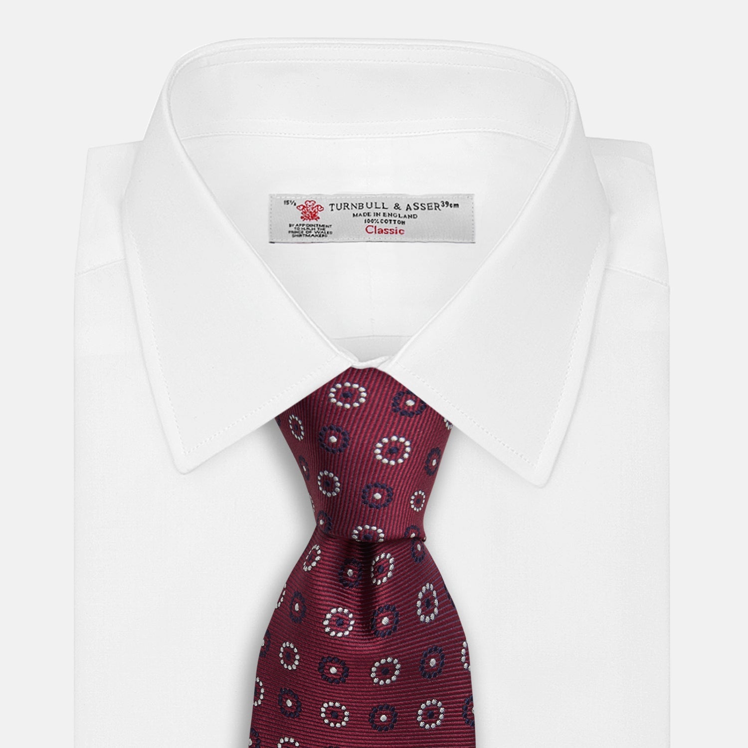 View 2 of product The Red Spheric Emblem Tie by Turnbull & Asser is a rolled-up maroon silk tie with a jacquard pattern of small white and purple circular dots, shown against a white background.