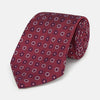 View 1 of product The Red Spheric Emblem Tie by Turnbull & Asser is a rolled-up maroon silk tie with a jacquard pattern of small white and purple circular dots, shown against a white background.