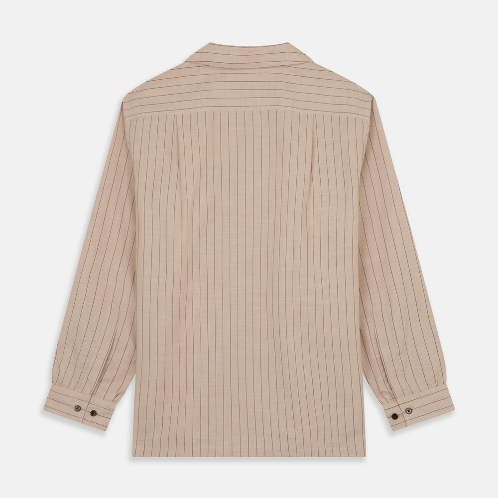 An older man in a light hat, Turnbull & Asser Beige Stripe Cotton Holiday Fit Shirt with Revere Collar & Single Button Cuff, and white pants leans casually against a tall concrete pillar outdoors, greenery blurred behind him.