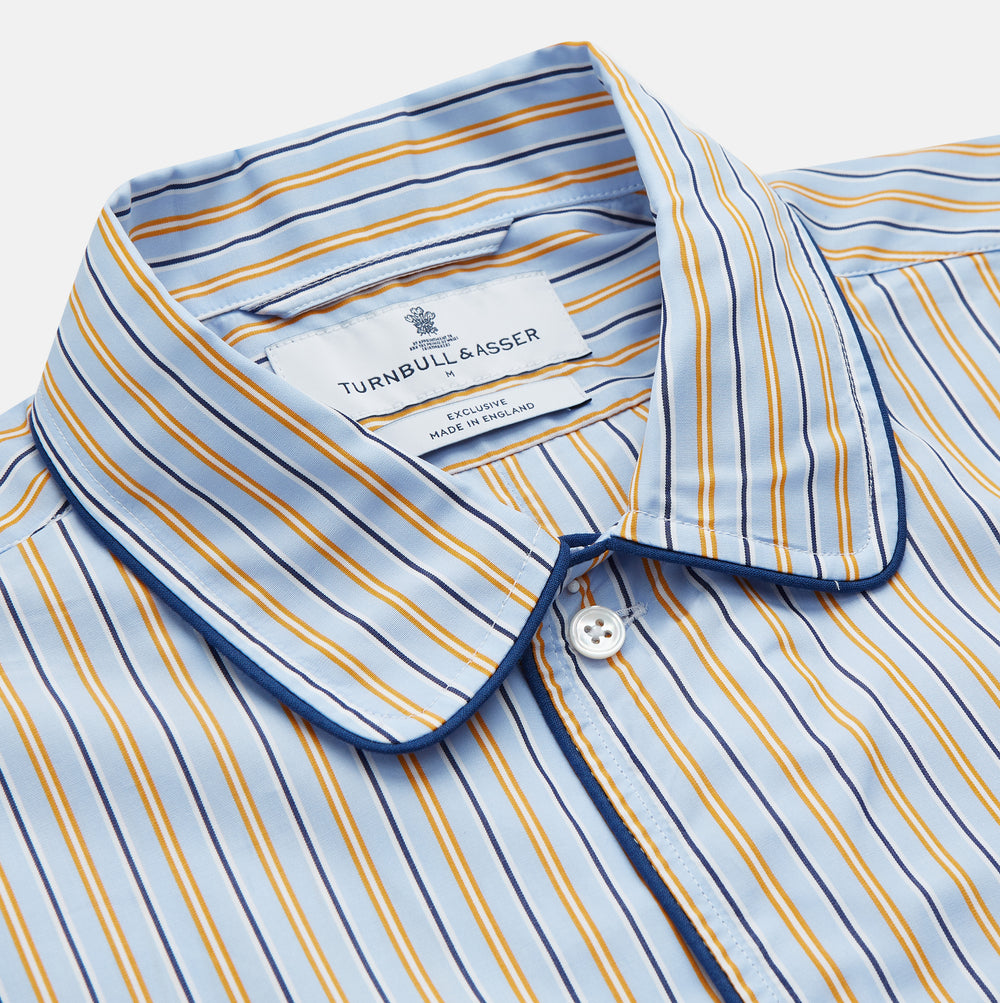 The Turnbull & Asser Blue, Orange and Navy Stripe Nightshirt is a loose-fitting shirt dress with vertical stripes, a pointed collar, chest pocket with blue trim, button-down front, long sleeves with cuffs, and a curved hem.