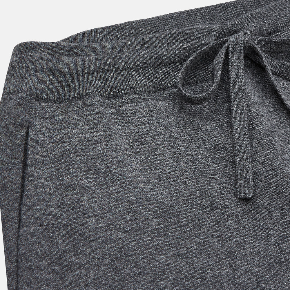 The Turnbull & Asser Grey Cashmere Knitted Lounge Pyjama Trousers feature an elastic waistband with drawstring, side pockets, and elastic cuffs at the ankles, shown laid flat on a white background.