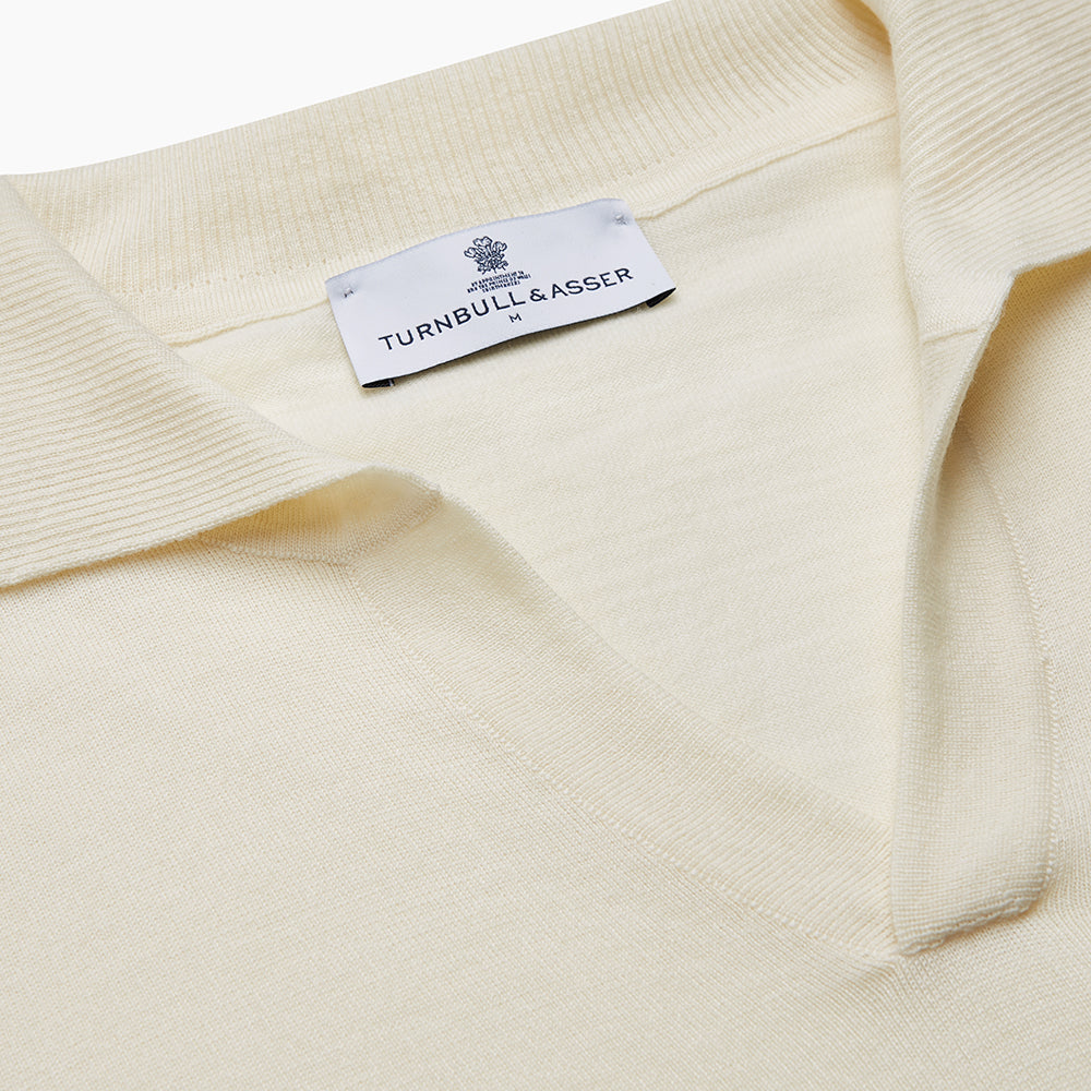 The Turnbull & Asser Ecru Merino Wool Roland Polo Shirt, made in Scotland, features soft merino wool, short sleeves, a relaxed open collar, and an inner neckline label. Shown here on a plain white background.